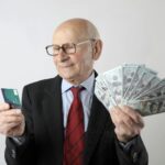 Elderly man in a suit holding a credit card and US dollar bills, representing finance and wealth.